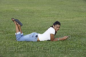 PictureIndia - Young woman laying on grass listening to MP3 player