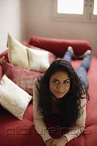 PictureIndia - Indian woman laying down on red sofa and smiling.