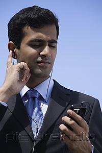 PictureIndia - Indian businessman listening to music, outside.