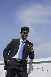 PictureIndia - Indian businessman reading text message outside.
