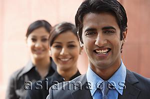 Asia Images Group - one businessman in foreground, two businesswomen in background, all smiling (horizontal)