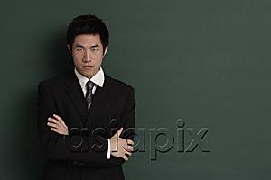 AsiaPix - Businessman standing against black wall with arms crossed