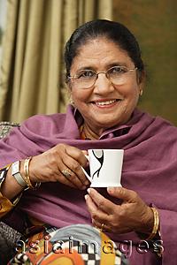 Asia Images Group - older woman with glasses holds cup of tea, smiles at camera