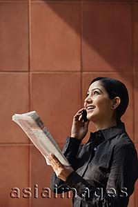 Asia Images Group - woman talking on phone, holding newspaper