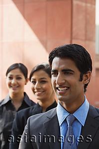 Asia Images Group - one businessman in foreground, two businesswomen in background, all smiling (vertical)