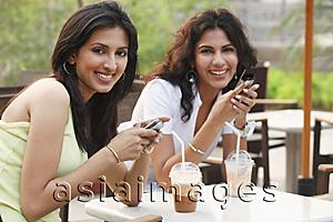 Asia Images Group - two young women having drinks,holding cell phones