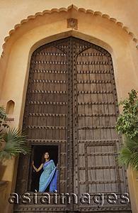 Asia Images Group - young woman standing at a huge wooden doorway
