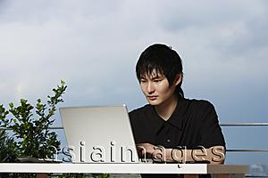 Asia Images Group - young man sitting outdoor using laptop