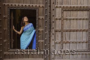 Asia Images Group - young woman in sari at window inside huge wooden doorway