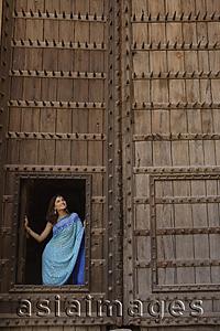 Asia Images Group - young woman standing at opening of huge wooden doorway