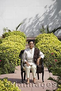Asia Images Group - woman sitting on chair outside, wearing salwar kameez and shawl