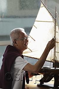AsiaPix - mature man working on model sail boat and smiling