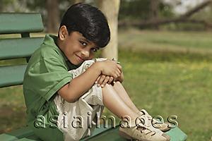 Asia Images Group - Little boy hugging knees on park bench