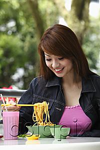 AsiaPix - Young woman sitting outside eating noodles