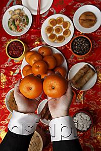 AsiaPix - Hands holding oranges over table with Chinese food