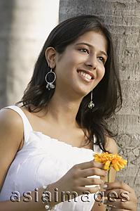 Asia Images Group - teen girl leaning against tree, with flower
