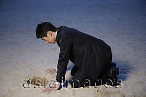 Asia Images Group - Businessman looking into hole in sand