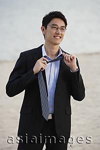 Asia Images Group - Businessman on beach, removing tie