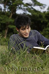 Asia Images Group - Young man reading in grass
