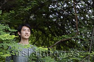 Asia Images Group - Young man standing in foliage