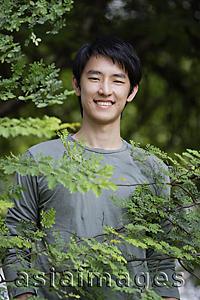Asia Images Group - Young man smiling behind foliage