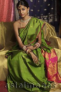 Asia Images Group - woman wearing sari, surrounded by sari fabric, decorated with henna tattoos, jewelry and bindi