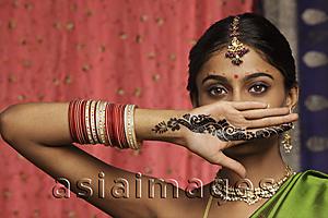 Asia Images Group - woman with hands decorated in henna, standing against wall of sari fabric