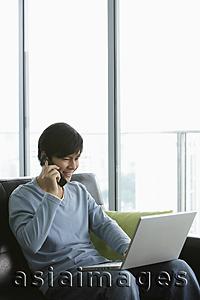 Asia Images Group - Young man talking on phone and working on laptop