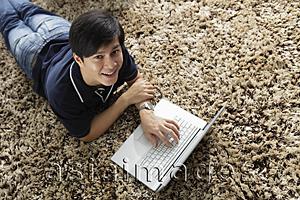 Asia Images Group - Young man laying on stomach working at lap top computer