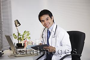 Asia Images Group - Doctor sitting at desk working on computer, smiling