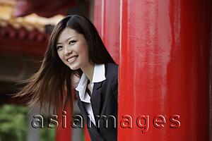 Asia Images Group - Young woman looking out from red pillars smiling