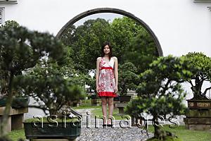 Asia Images Group - Young woman standing with bonsai trees