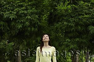 Asia Images Group - Young woman looking up at bamboo trees