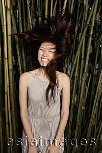 Asia Images Group - Young woman flipping her hair in front of bamboo