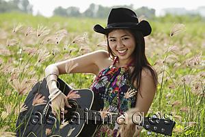Asia Images Group - smiling woman playing guitar in grassy field