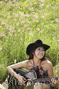 Asia Images Group - smiling woman playing guitar outside on the grass