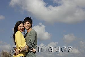 Asia Images Group - young couple hugging outside with blue sky and clouds as background