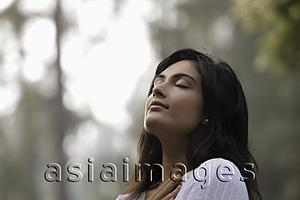 Asia Images Group - Back lit head shot of young woman with eyes closed outdoors