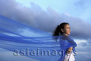 Asia Images Group - Young girl holding blue cloth blowing in the wind with blue sky background