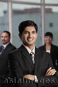 Asia Images Group - Indian man smiling with arms folded. Colleagues behind him.