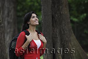 Asia Images Group - Young woman wearing a back pack looking up at trees and smiling