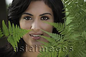Asia Images Group - Head shot of young woman looking through ferns and smiling