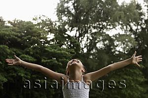 Asia Images Group - Young girl with arms outstretched looking up at the sky smiling, trees background