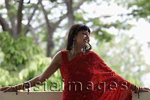 Asia Images Group - Indian woman wearing red sari leaning on balcony, smiling
