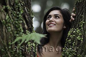Asia Images Group - Head shot of young woman looking through a tree and smiling