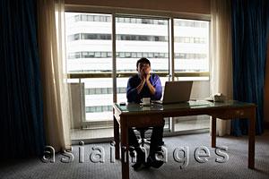 Asia Images Group - Young man sitting at desk with lap top looking stressed