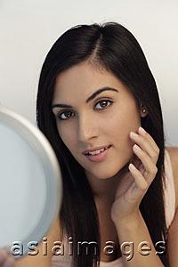 Asia Images Group - Head shot of young woman holding mirror and touching her face