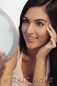 Asia Images Group - Young woman looking at mirror smiling while touching her face
