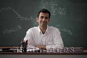 Asia Images Group - Young man sitting at his desk smiling with chalk board behind
