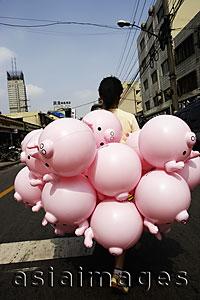 Asia Images Group - Woman walking with pink pig balloons down the street of Shanghai, China